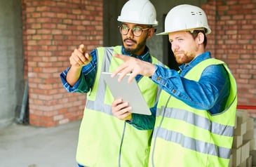 A pair of construction workers discussing project implementation and the time-saving benefits of using construction management software. 