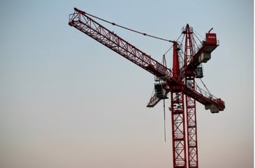 An overhead red crane in front of a sunset pointing to the left representing the future of the construction industry. 