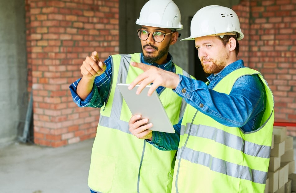 A pair of construction workers discussing project implementation and the time-saving benefits of using construction management software. 