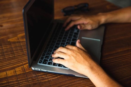 A contractor typing on a laptop on a wooden desk using construction management software. 